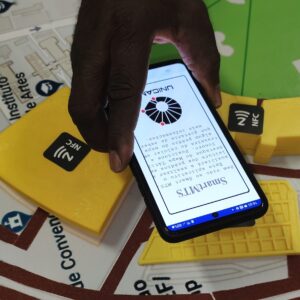 Detalhe de celular com o app SmartMTS próximo de um prédio em 3D com sensor NFC em mapa da Unicamp.